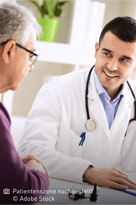 Freundlich lächelnder junger Arzt schaut seinen älteren Patienten aufmunternd an: Mastozytose ist nicht heilbar, die Symptome lassen sich aber lindern.