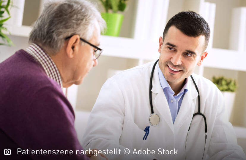 Freundlich lächelnder junger Arzt schaut seinen älteren Patienten aufmunternd an: Mastozytose ist nicht heilbar, die Symptome lassen sich aber lindern.