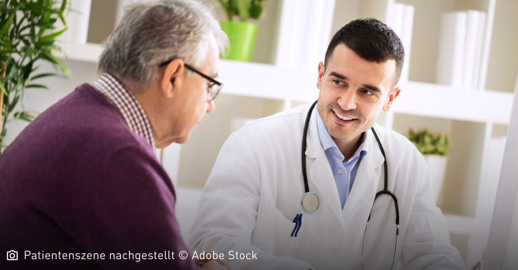 Freundlich lächelnder junger Arzt schaut seinen älteren Patienten aufmunternd an: Mastozytose ist nicht heilbar, die Symptome lassen sich aber lindern.